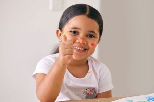 Smiling young girl with thumbs up while fingerpainting