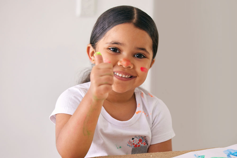 Smiling young girl with thumbs up while fingerpainting